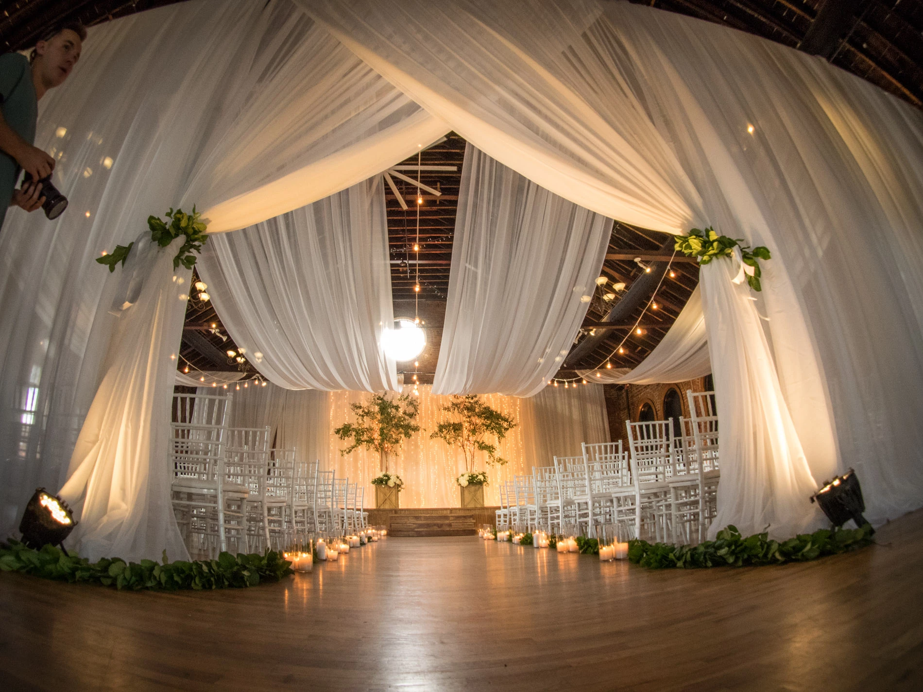 A close-up of wedding bouquets in glass vases on a black marble table, featuring blush and white roses, eucalyptus, and thistle accents, with a softly lit card box in the background.