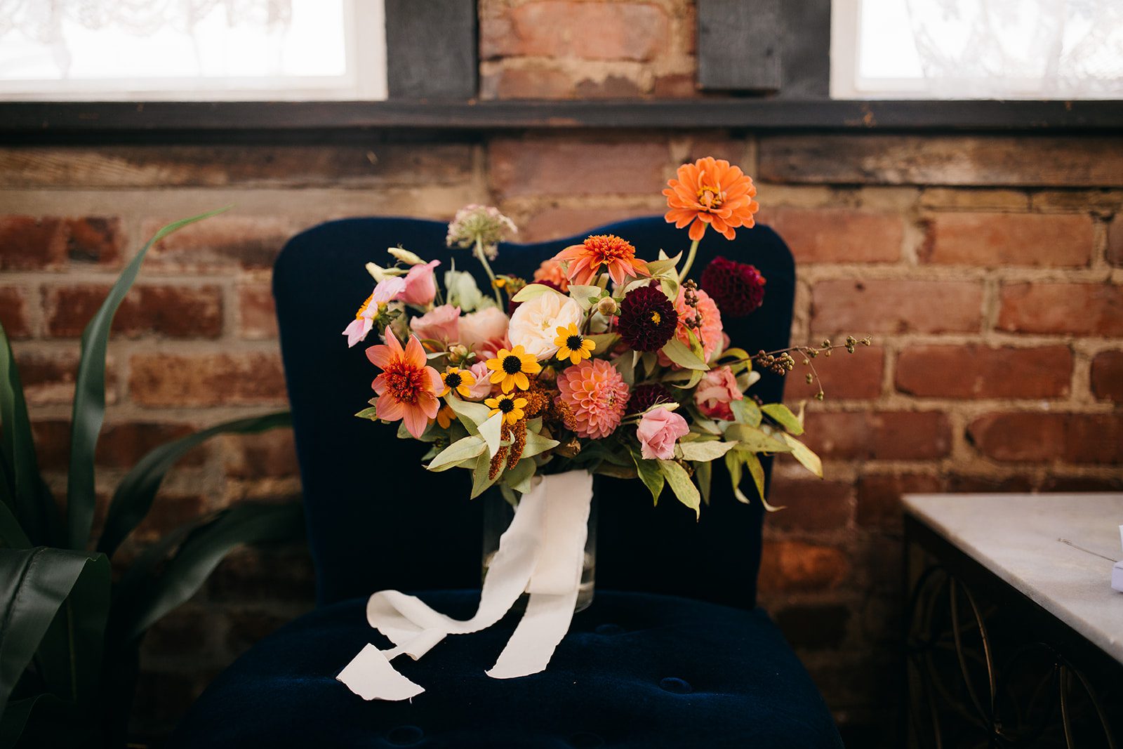Wedding planning resources showcasing colorful flowers sitting in a dark navy chair with a brick wall background.