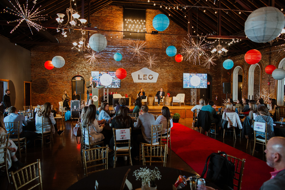A close-up of wedding bouquets in glass vases on a black marble table, featuring blush and white roses, eucalyptus, and thistle accents, with a softly lit card box in the background.